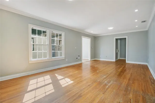 a view of an empty room with wooden floor and a window