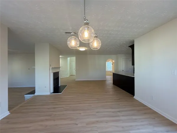 a view of empty room with wooden floor and kitchen