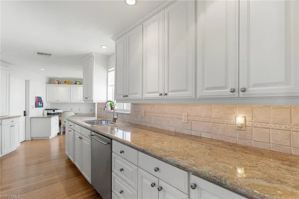 a kitchen with granite countertop a sink white cabinets and stainless steel appliances