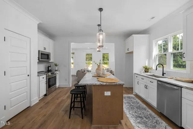 a kitchen with stainless steel appliances kitchen island granite countertop a stove a sink dishwasher a refrigerator white cabinets and wooden floor next to a window