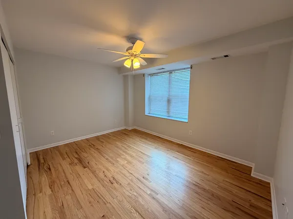 an empty room with wooden floor chandelier fan and windows