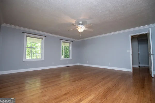 an empty room with wooden floor chandelier fan and windows