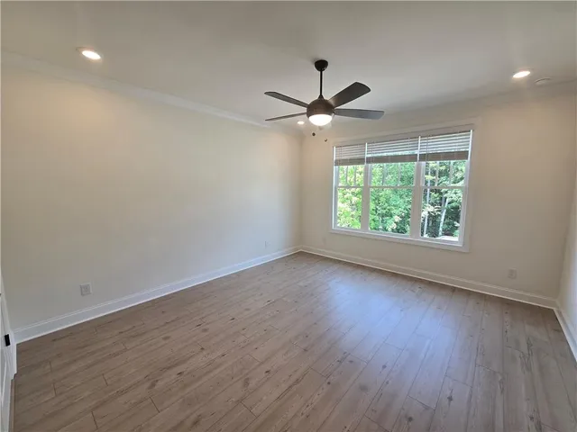 an empty room with wooden floor ceiling fan and windows