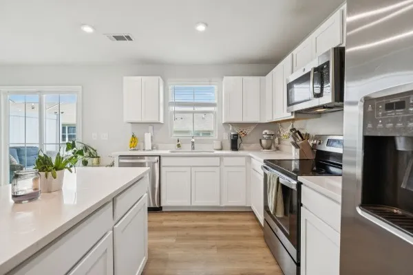 a kitchen with stainless steel appliances a sink dishwasher a stove top oven a refrigerator with white cabinets and wooden floor