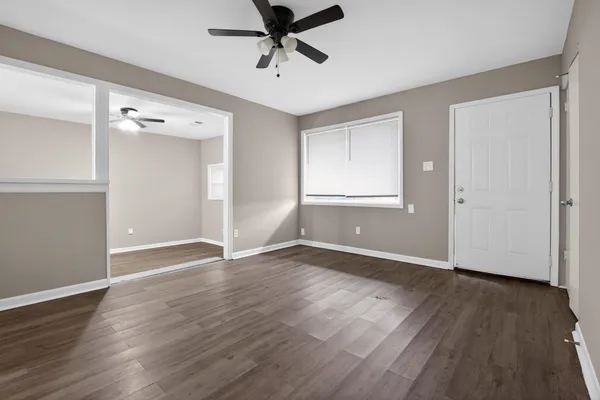 a view of an empty room with wooden floor and a ceiling fan
