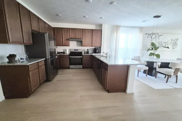 a kitchen with stainless steel appliances kitchen island granite countertop a refrigerator a sink dishwasher a stove with wooden cabinets and floor
