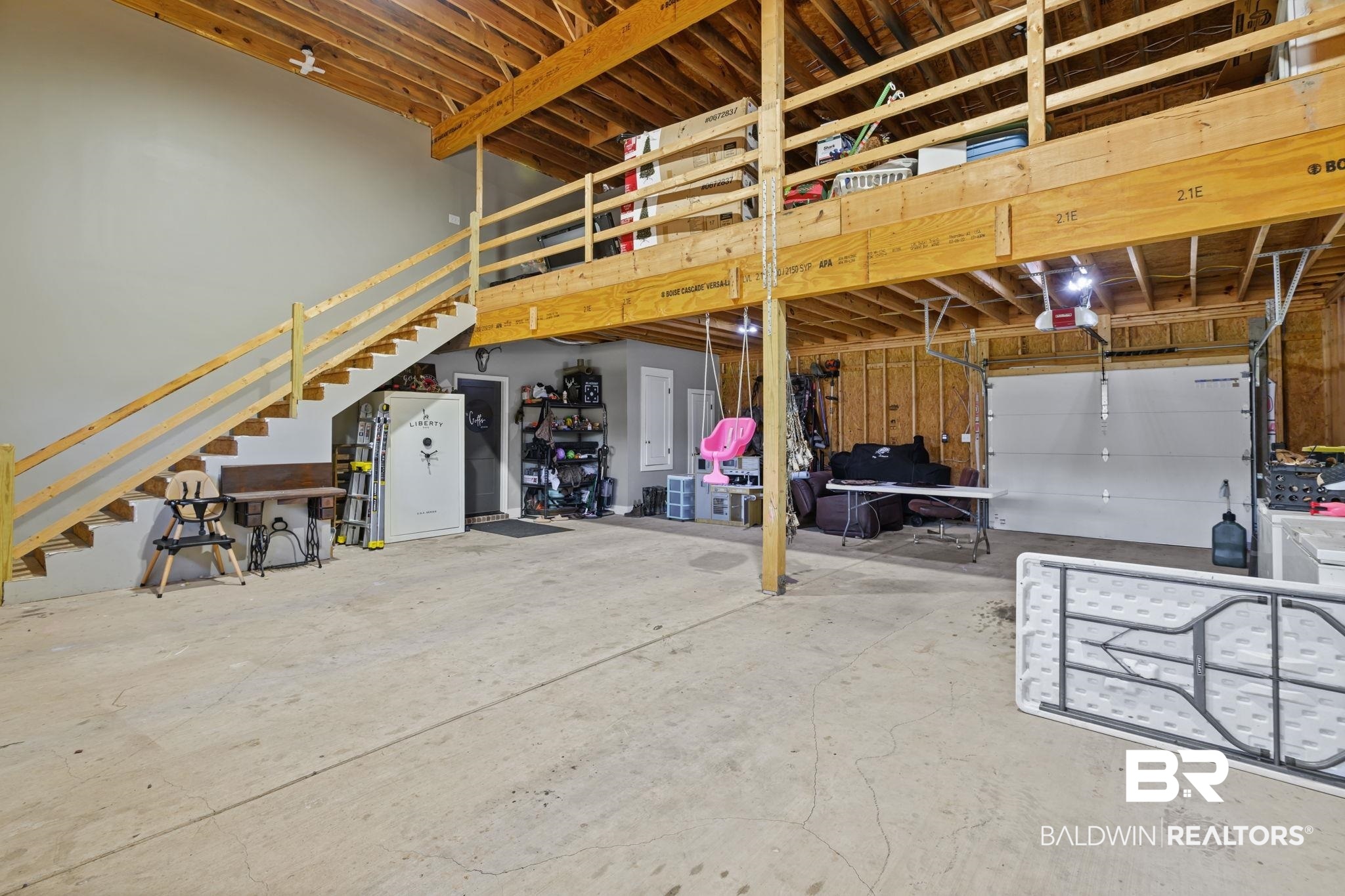 11025 Creax Road Axis, AL 36505 - Photo 34 of 45 Spacious garage interior featuring a concrete floor, exposed wood beam ceiling, and a prominent second-story loft with wood railing