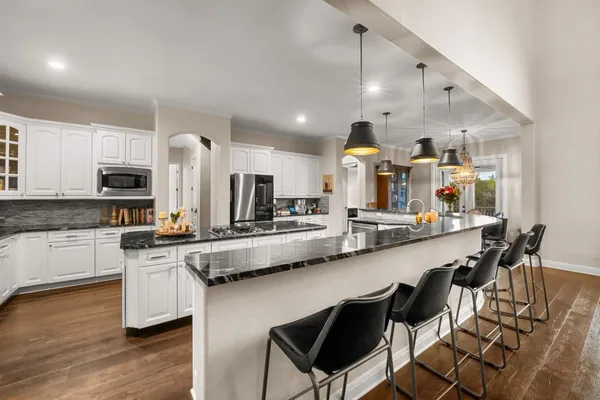 a large kitchen with stainless steel appliances granite countertop a lot of white cabinets a sink a stove and a refrigerator