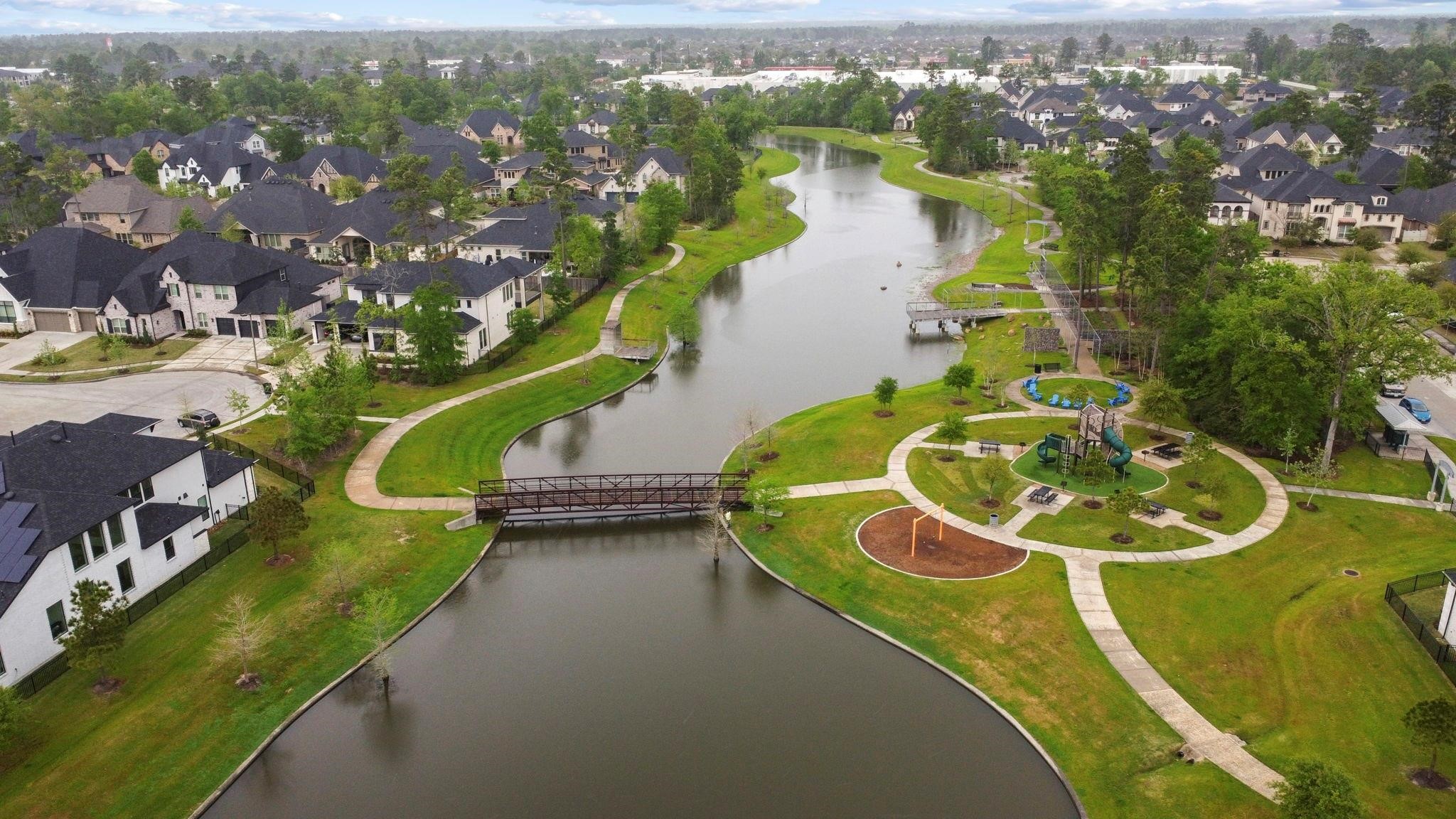 17465 Buckeye Branch Conroe, TX 77385 - Photo 44 of 47 This aerial photo showcases a serene residential neighborhood featuring a picturesque waterway, lush greenery, and well-maintained walking paths. The area includes a charming footbridge and a playground, creating a family-friendly environment. The homes are spacious and modern, offering a peaceful and inviting community atmosphere.