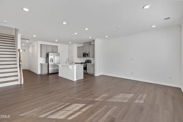 an empty room with wooden floor and kitchen view