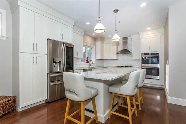 a kitchen with stainless steel appliances granite countertop a stove a refrigerator a kitchen island a dining table and chairs with wooden floor