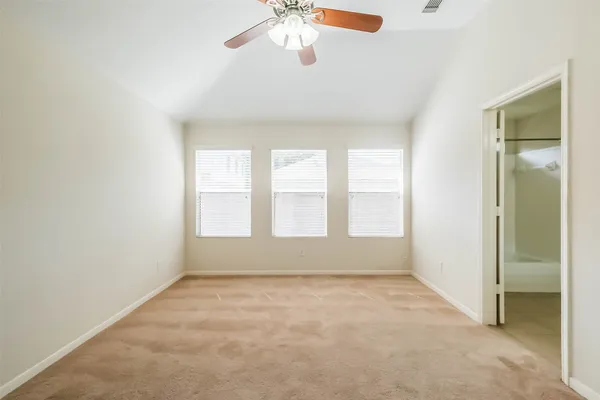 an empty room with chandelier fan and windows