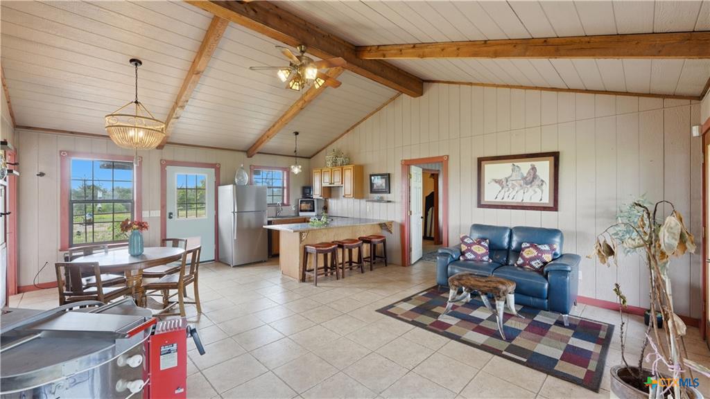 127 Offer Llano, TX 78643 - Photo 10 of 40 Open-concept living space featuring vaulted wood-paneled ceilings with exposed beams, light-toned tile flooring, and a kitchen island with seating
