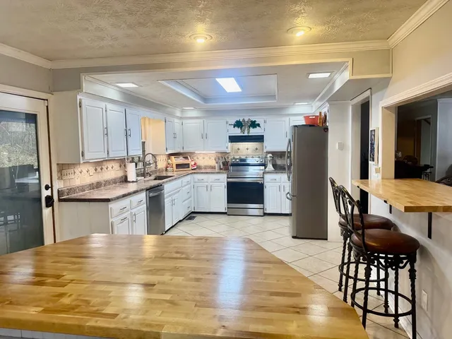 a kitchen with stainless steel appliances granite countertop a refrigerator a stove top oven a sink dishwasher and white cabinets with wooden floor