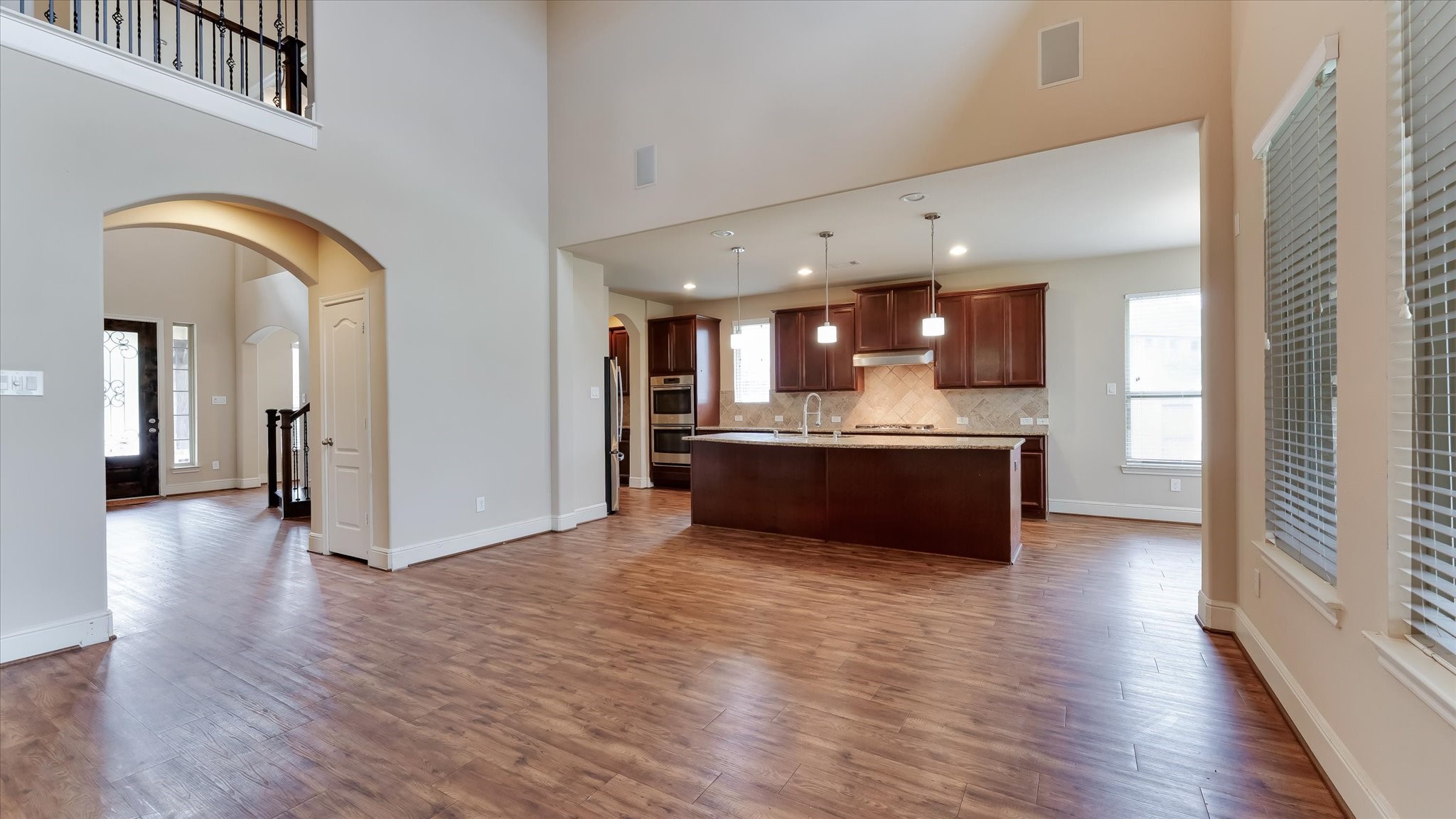 17211 Green Darter Conroe, TX 77385 - Photo 12 of 48 This spacious, open-concept home features a stunning kitchen with modern cabinetry, a large island, and pendant lighting. The wood floors complement the neutral walls, and the high ceilings enhance the airy feel. Large windows provide ample natural light, and the arched doorway adds an elegant touch.