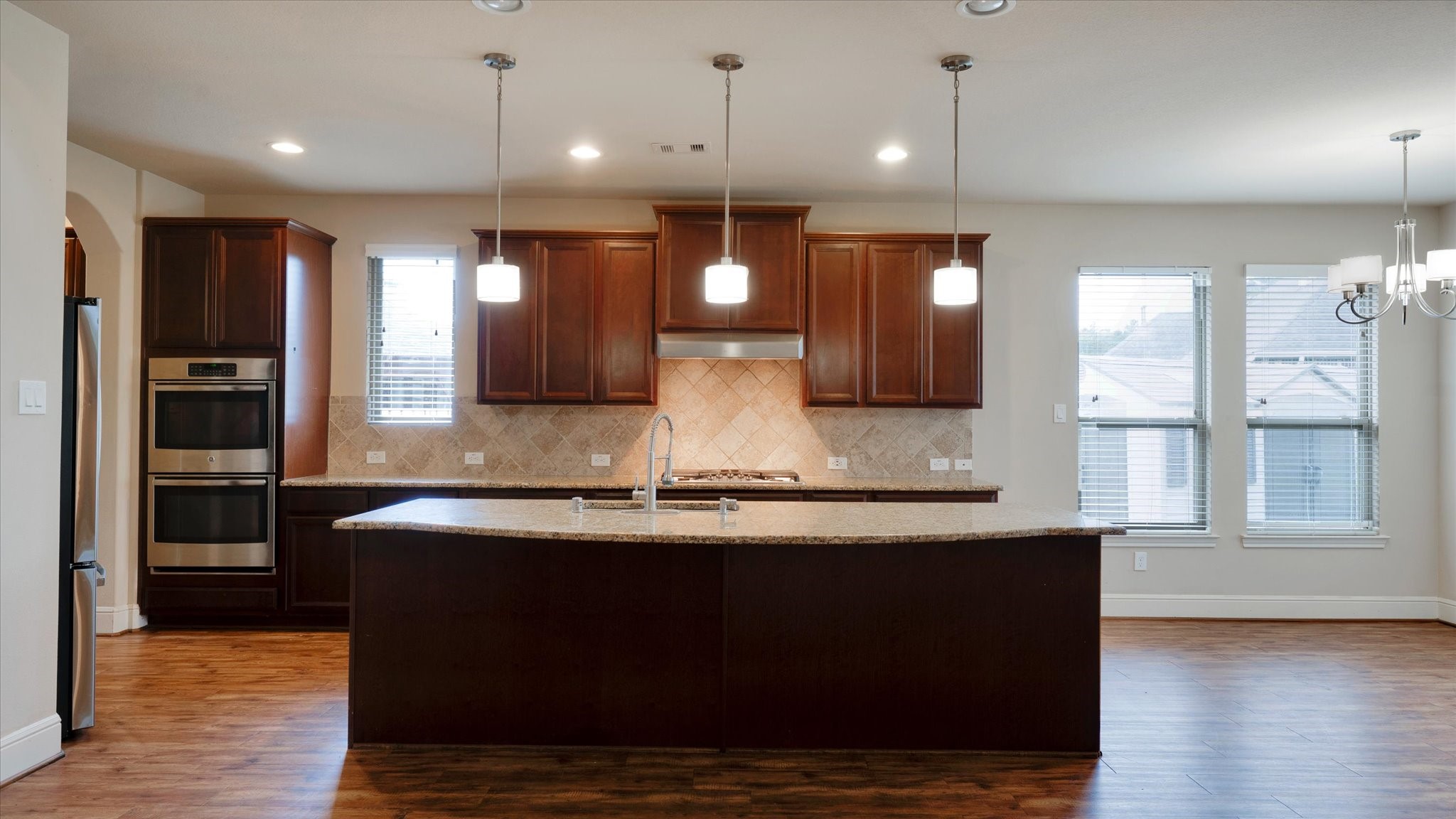 17211 Green Darter Conroe, TX 77385 - Photo 13 of 48 This kitchen features a spacious open layout with modern dark wood cabinets, a large center island, granite countertops, and stainless steel appliances. It has ample natural light from multiple windows and elegant pendant lighting.