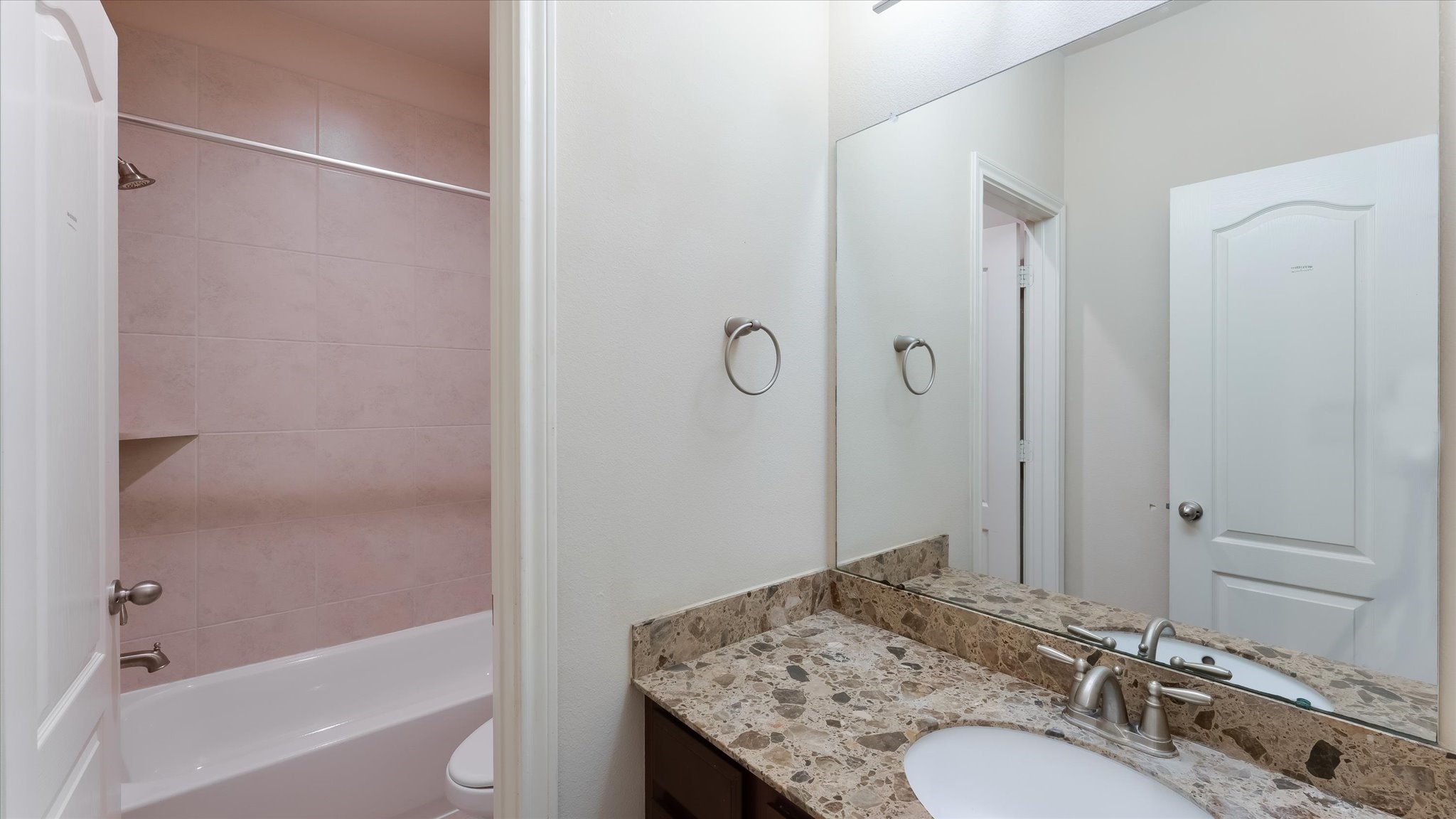 17211 Green Darter Conroe, TX 77385 - Photo 28 of 48 The downstairs hallway full bathroom has a granite countertop, an under-mount sink, and a large mirror. It features a bathtub with tiled walls and a shower curtain rod.