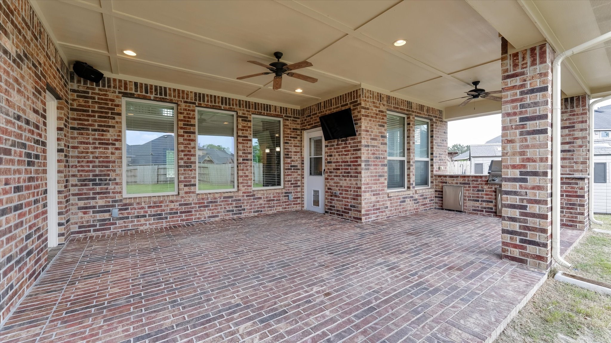 17211 Green Darter Conroe, TX 77385 - Photo 4 of 48 This spacious covered patio features a brick finish, ceiling fans, and built-in speakers, creating an ideal space for outdoor entertaining. Large windows provide a view of the backyard, enhancing the open, airy feel.