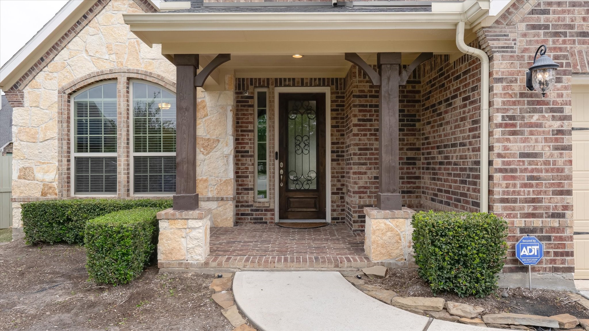 17211 Green Darter Conroe, TX 77385 - Photo 7 of 48 Beautiful brick and stone entryway featuring a covered porch with wooden columns, neatly trimmed hedges, and a decorative front door with ironwork, exuding a welcoming and secure ambiance.