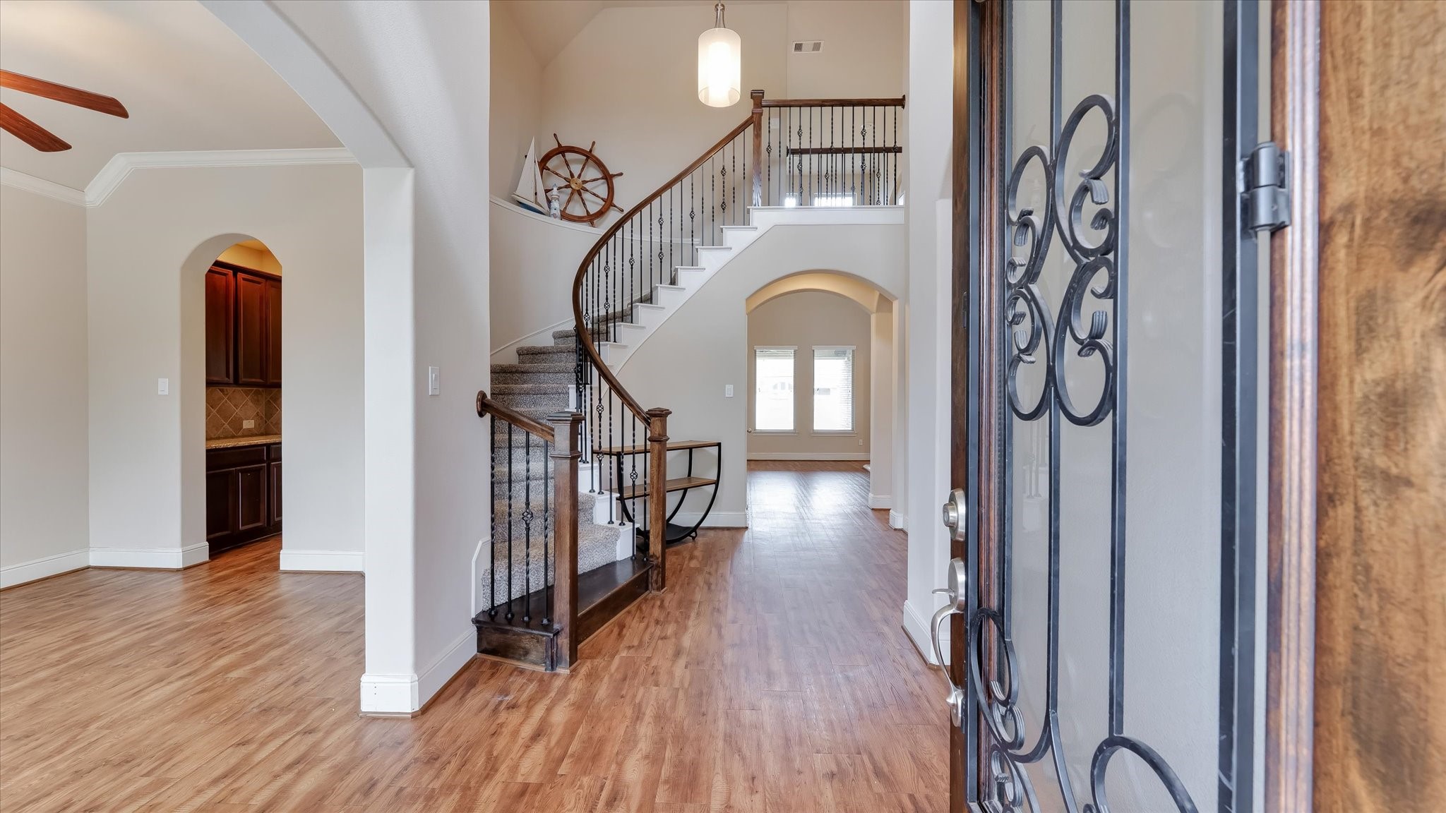 17211 Green Darter Conroe, TX 77385 - Photo 8 of 48 This inviting entryway features a beautiful wooden staircase with wrought-iron balusters, leading to an open, airy space. The wood floors add warmth, while the high ceilings and arched doorways enhance the elegance. A glimpse of the living room and large windows in the background promises ample natural light.