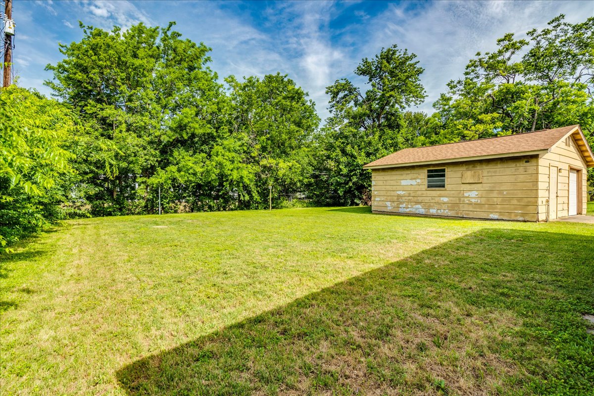 6626 Isabelle Drive Austin, TX 78752 - Photo 24 of 27 Expansive grassy yard with mature perimeter trees and a detached garage featuring dual bay doors and a side window
