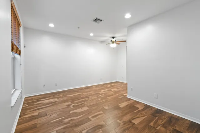an empty room with a chandelier fan and wooden floor