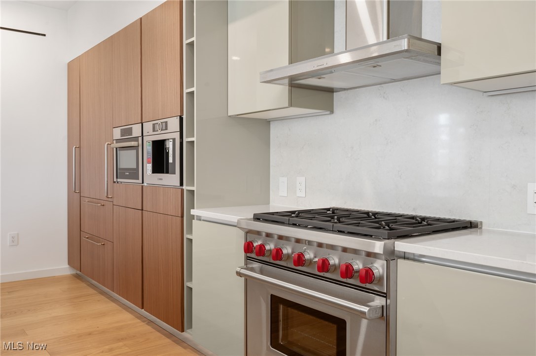 22700 Lake Road, Unit 204 Rocky River, OH 44116 - Photo 7 of 31 Kitchen with premium stove, wall chimney exhaust hood, light wood-type flooring, modern cabinets, and backsplash