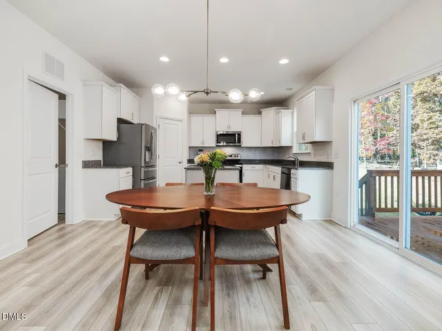 a kitchen with stainless steel appliances a dining table chairs wooden floor and a large window