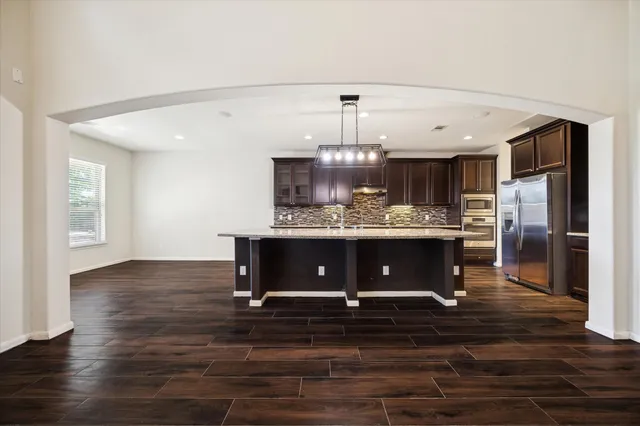 a room with kitchen island stainless steel appliances wooden floor and a counter top space