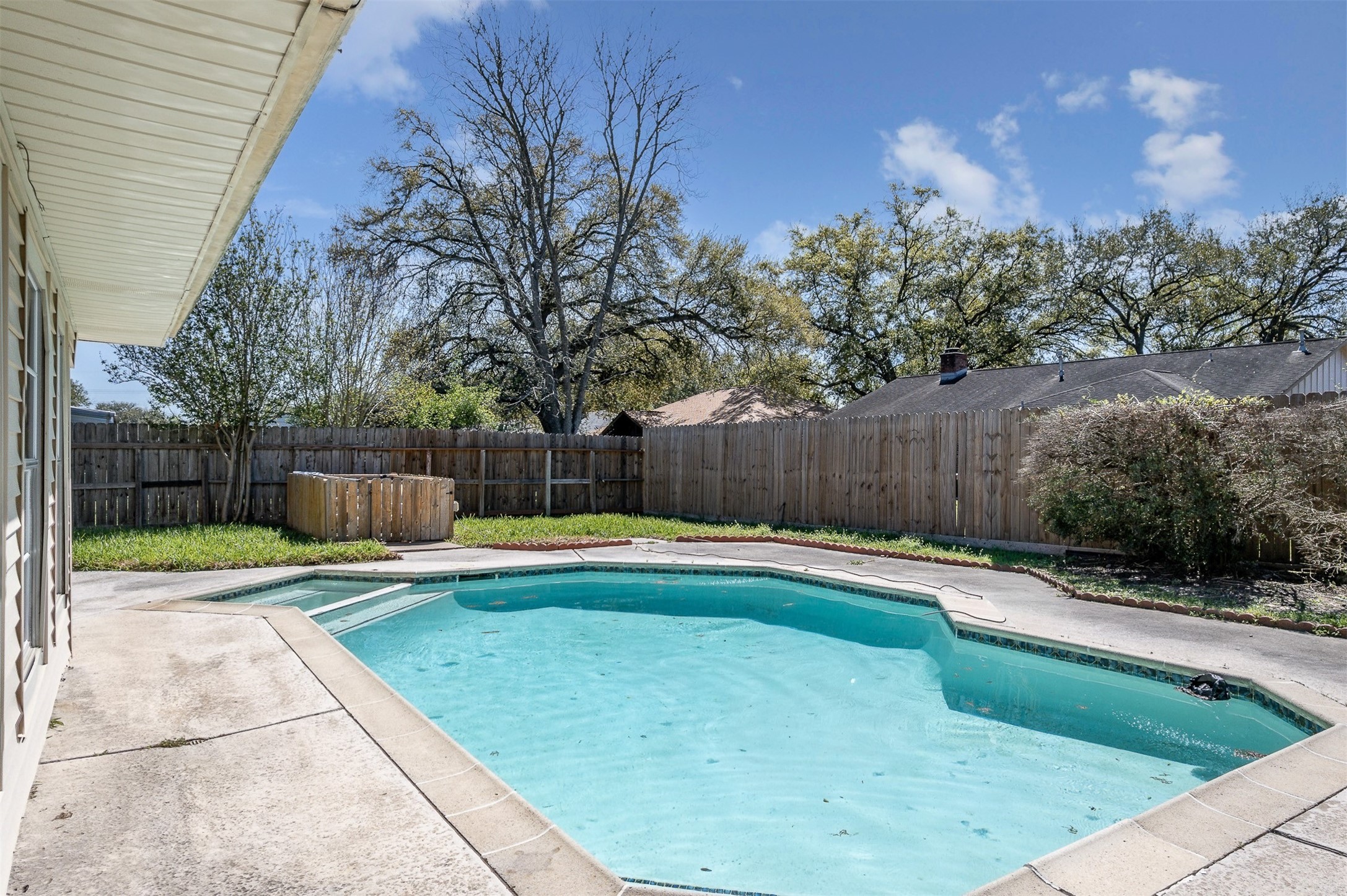 1603 East Baker Road Baytown, TX 77521 - Photo 24 of 26 This backyard features a clean, inviting pool surrounded by a concrete patio. It's enclosed by a wooden fence for privacy, with mature trees providing shade and greenery.