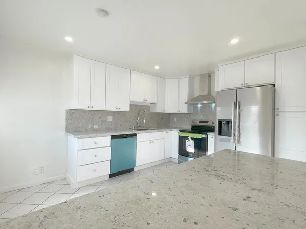 a kitchen with granite countertop a refrigerator stove oven and white cabinets