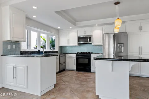 a kitchen with granite countertop a refrigerator a sink and white cabinets