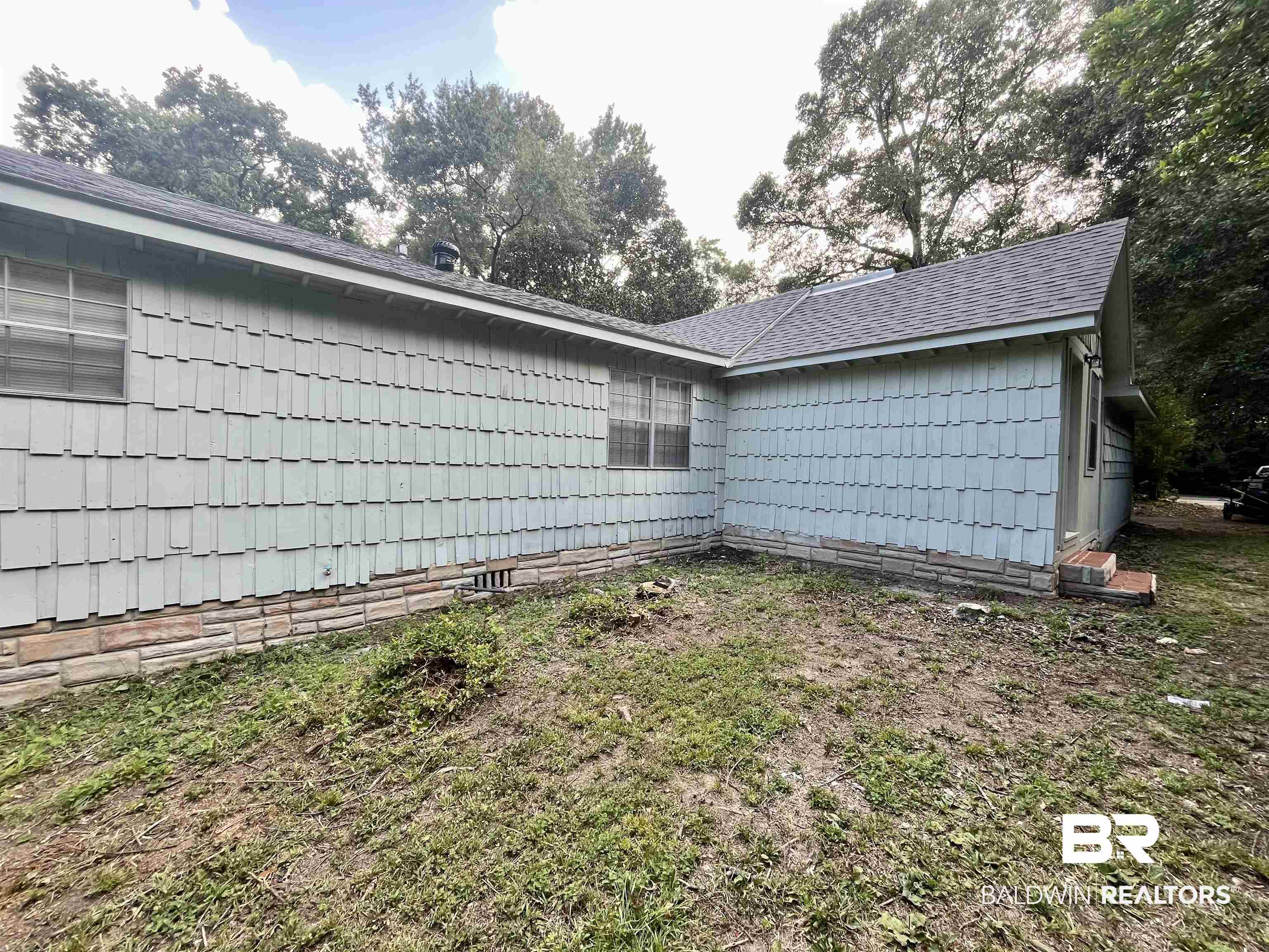 3105 Bryant Road Mobile, AL 36605 - Photo 37 of 39 Exterior featuring shingle siding, a stone foundation, a gabled roofline, and mature trees
