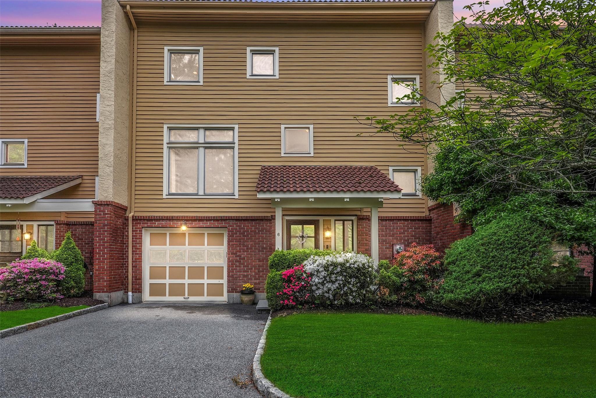 View of front facade featuring a garage, driveway, brick siding, and a yard