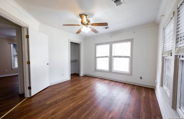 an empty room with wooden floor fan and windows