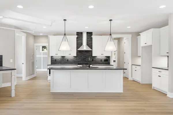 a large kitchen with granite countertop a stove a sink a center island a refrigerator and a wooden floor