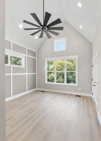 an empty room with wooden floor fan and windows