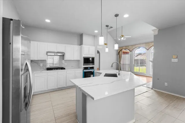 a kitchen with stainless steel appliances kitchen island granite countertop a refrigerator a sink a stove and white cabinets with wooden floor