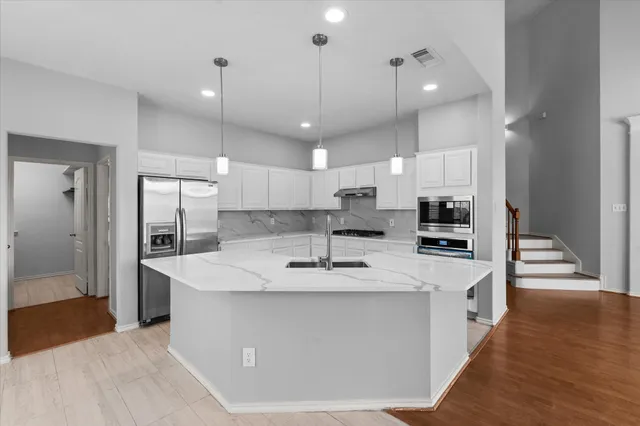 a large kitchen with stainless steel appliances kitchen island a stove a refrigerator a oven and a sink with wooden floor