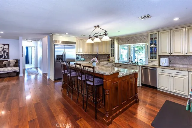 a kitchen with stainless steel appliances granite countertop a stove a sink dishwasher a microwave oven and a dining table with wooden floor