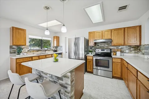 a kitchen with a stove a sink a kitchen island with wooden cabinets and chairs