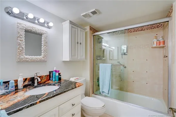 a bathroom with a granite countertop sink a toilet a mirror a vanity and shower
