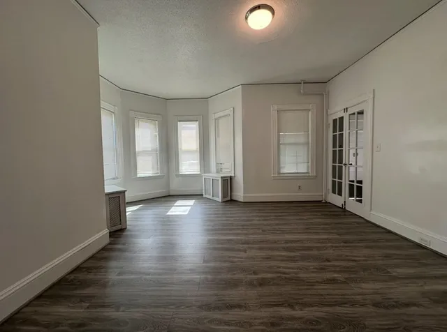an empty room with wooden floor and windows with curtains