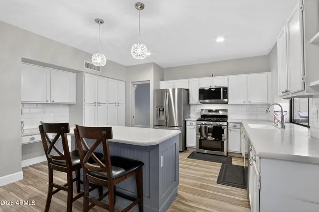 a kitchen with stainless steel appliances kitchen island granite countertop a sink a stove a refrigerator with white cabinets and wooden floor