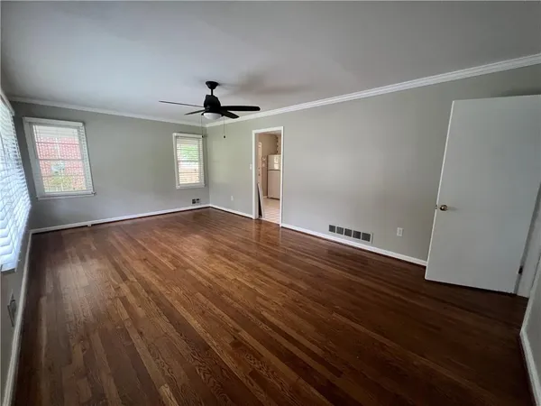 an empty room with wooden floor chandelier fan and windows