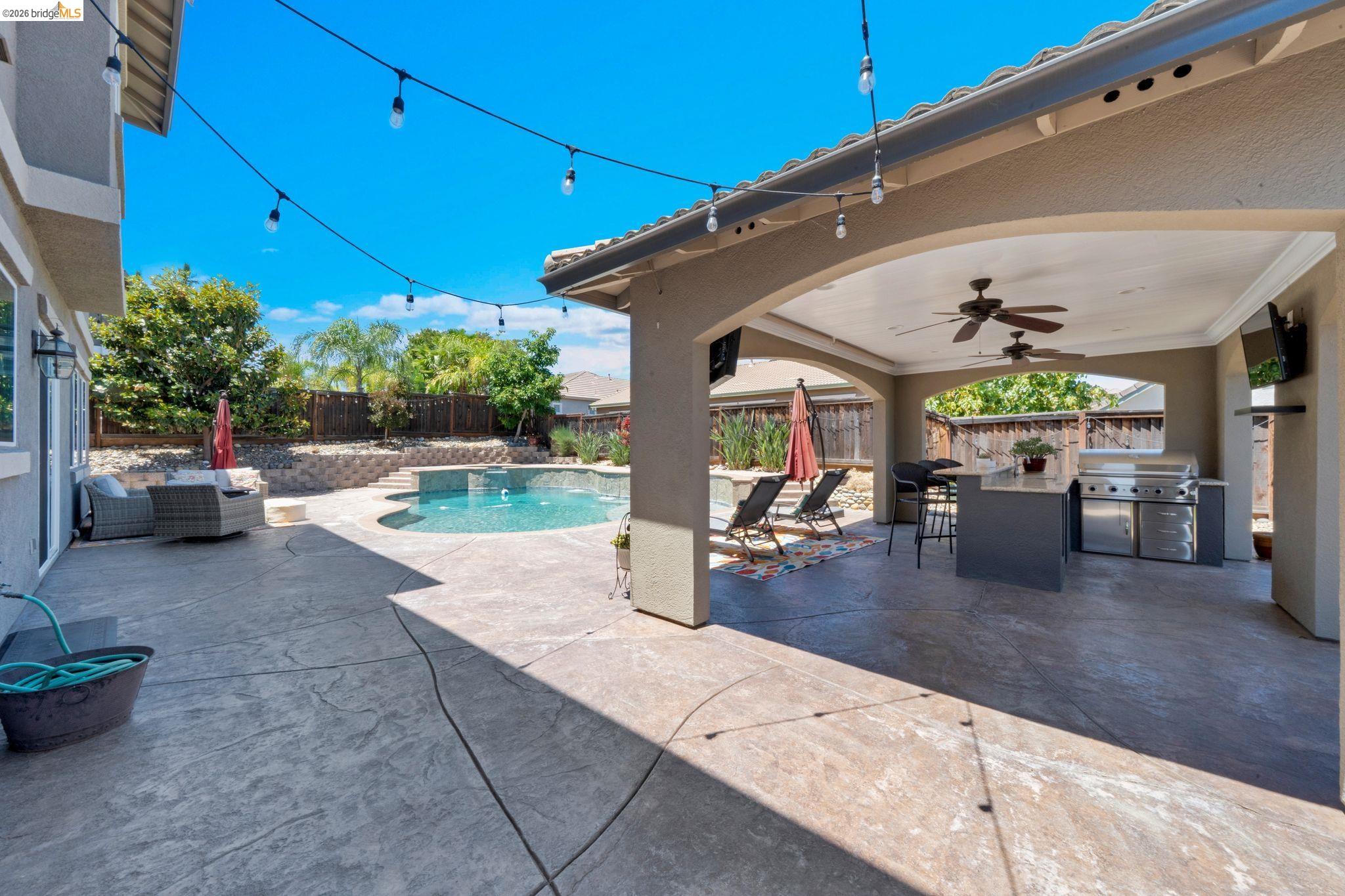 2513 Winged Foot Road Brentwood, CA 94513 - Photo 36 of 45 Expansive stamped concrete patio featuring a covered outdoor kitchen, a built-in swimming pool, and a tiered retaining wall