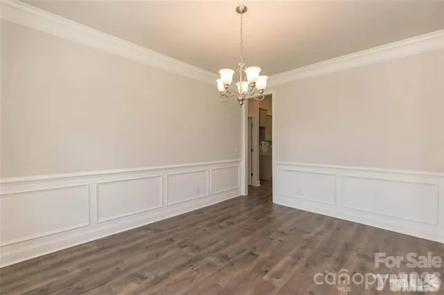a view of a room with wooden floor chandeliers and kitchen view
