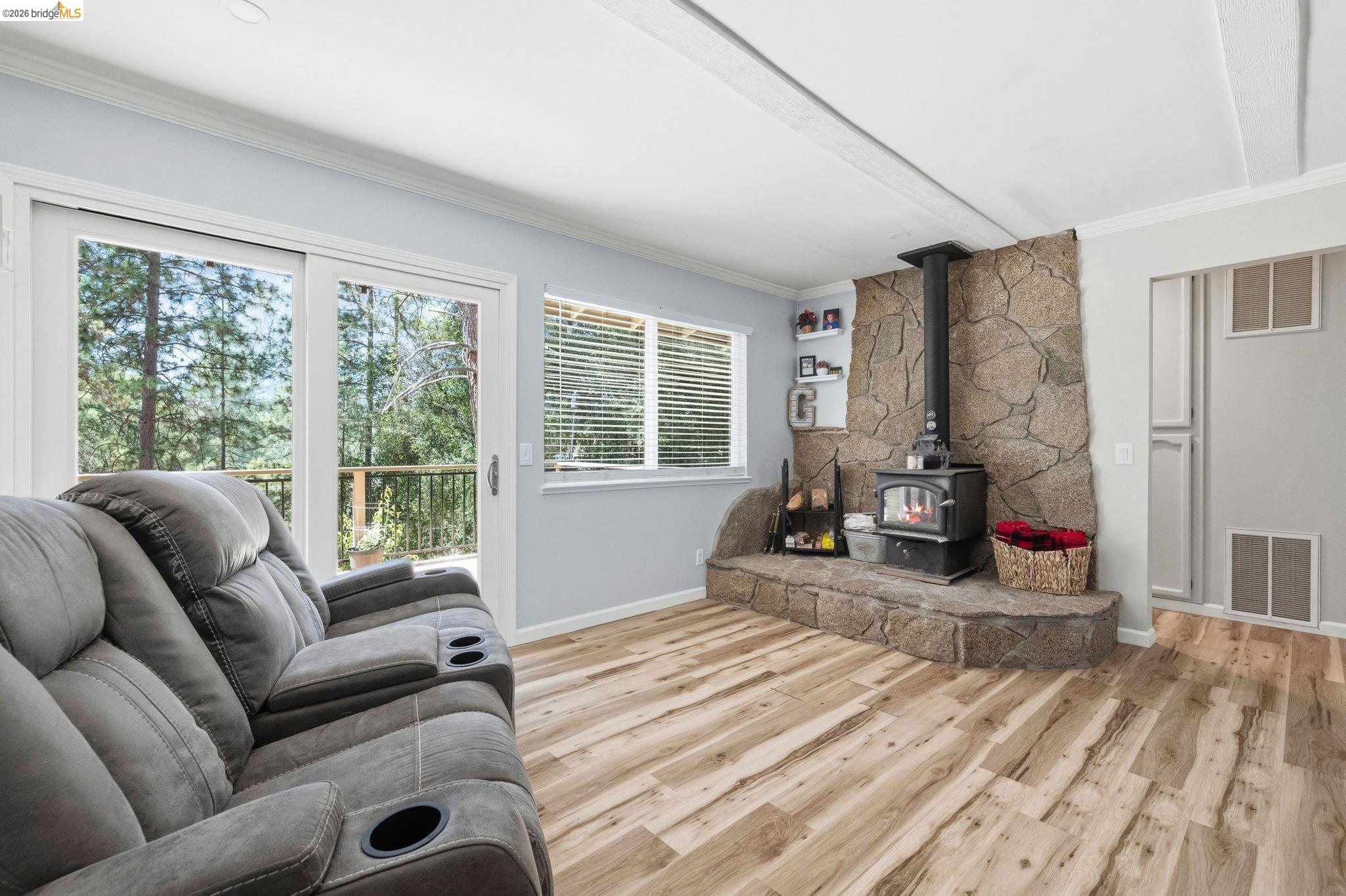 19059 Raboul Court Groveland, CA 95321 - Photo 7 of 21 Living area featuring a stone-clad wood-burning stove with a raised hearth, wood-finish flooring, and light-toned wall paint