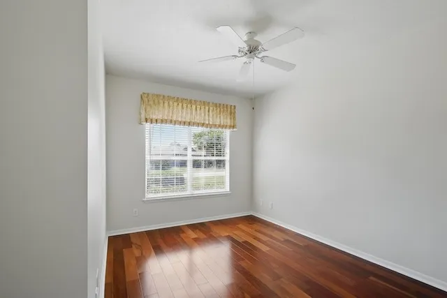 an empty room with wooden floor fan and windows