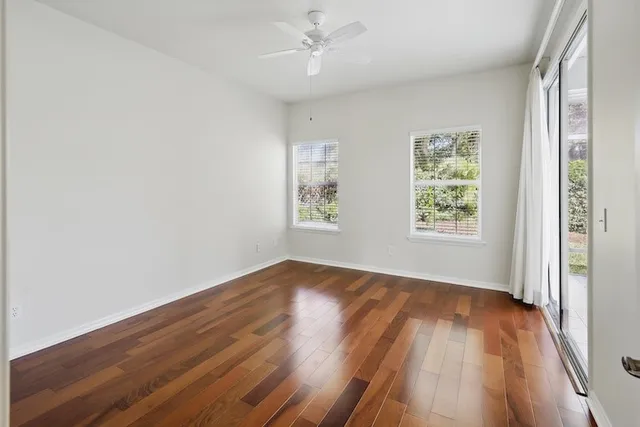 an empty room with wooden floor chandelier fan and windows